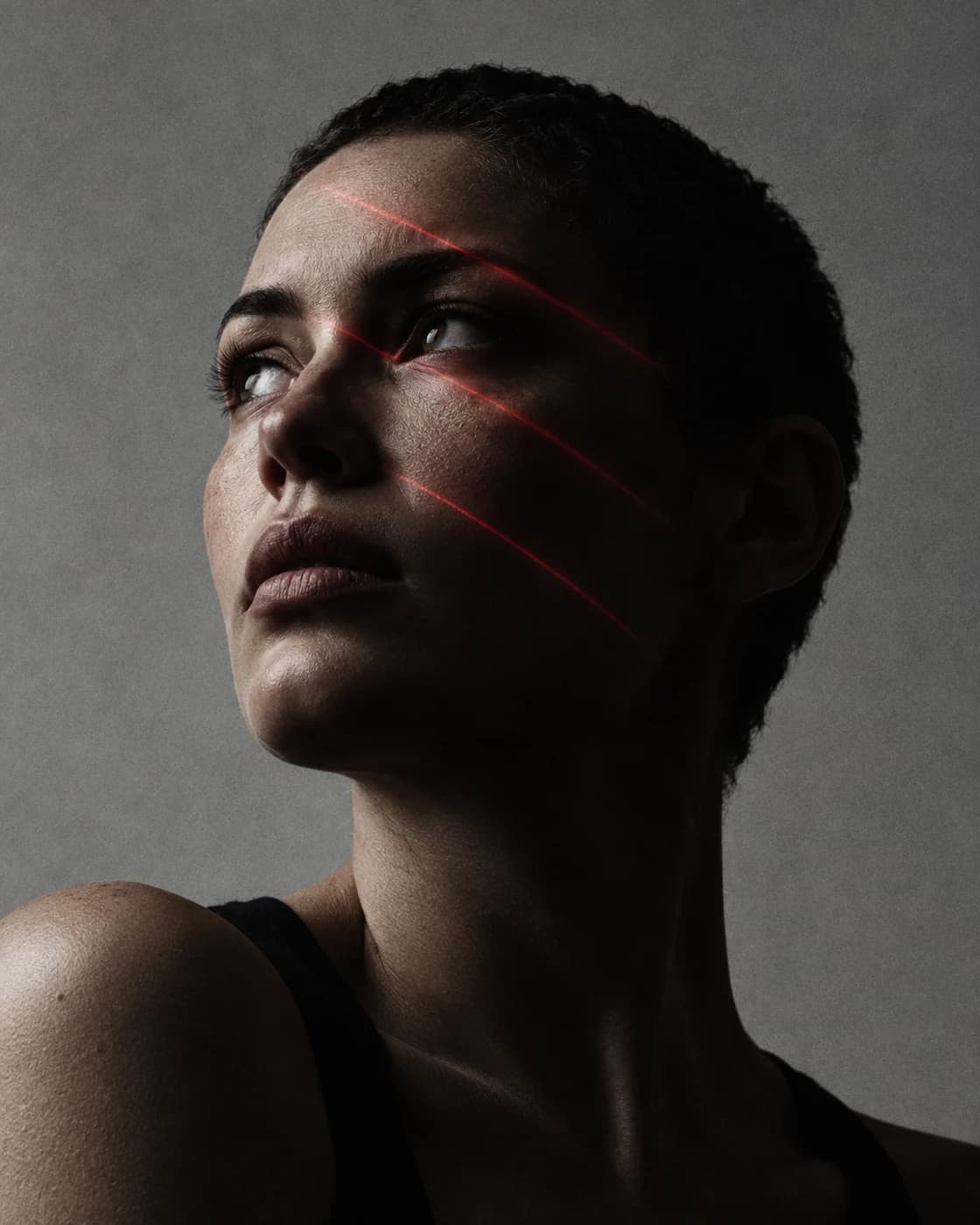 Conceptual portrait of a woman looking upward with restrained red light tracing her face.